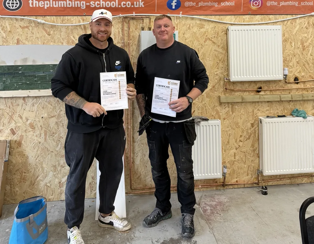 Two learners holding their Plumbing School course certificates